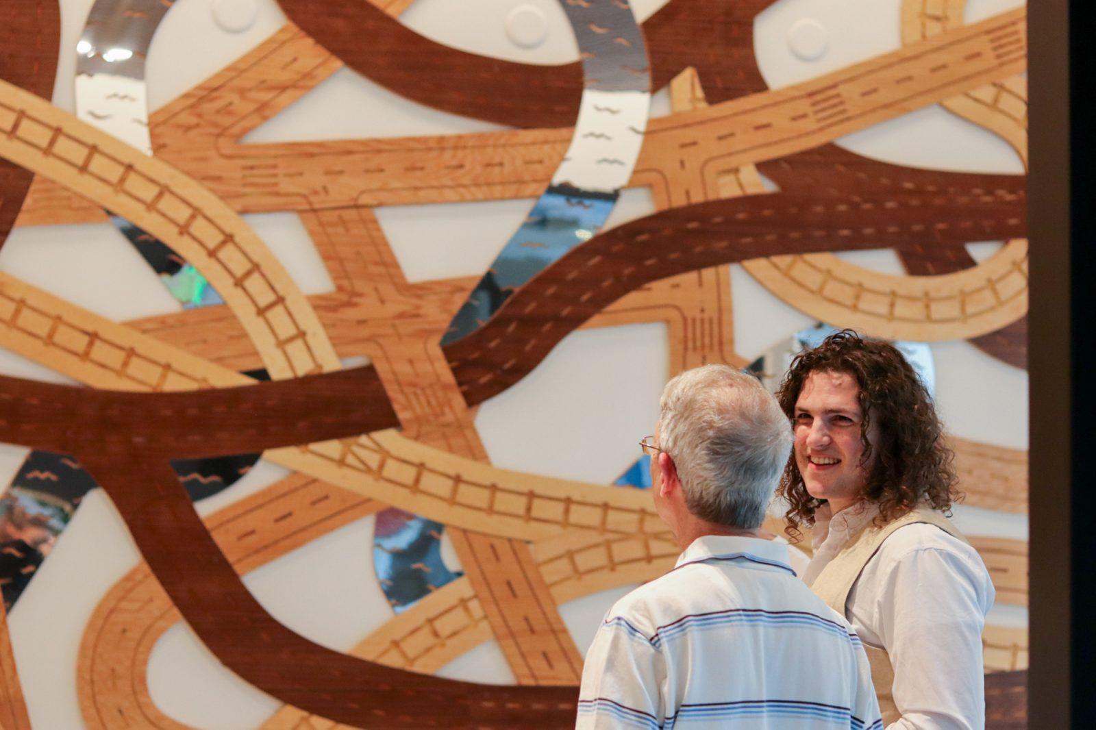 Alexander Golob describes his art installation, “Woven City,” to an attendee at its inaugural reception on Thursday night. “Woven City” took inspiration from Boston’s transportation infrastructure and was commissioned by The Hamilton Company for an apartment building in Packard’s Corner. RACHEL FEINSTEIN/DFP PHOTOGRAPHER