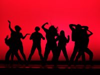A red backdrop silhouettes dance group, BU Vibes.