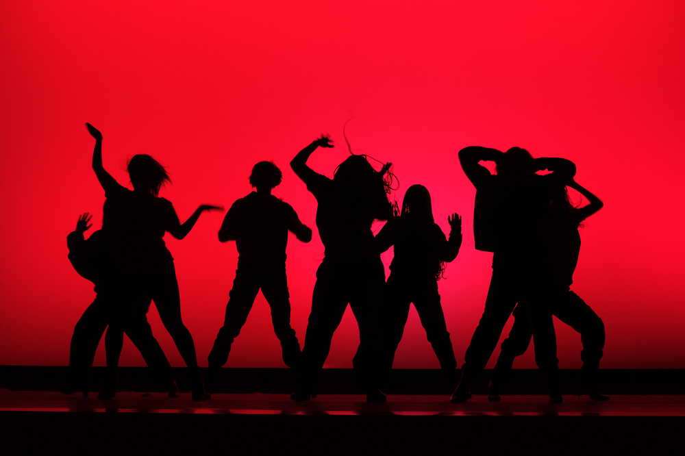 A red backdrop silhouettes dance group, BU Vibes.