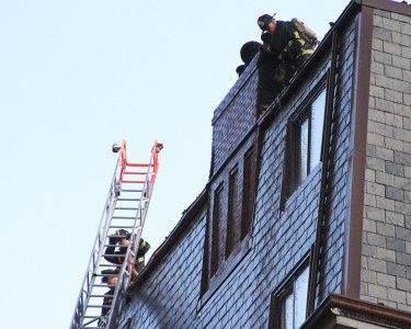 Firefighters work atop 182 Beacon St. after a fire on the roof of the building Monday evening. PHOTO BY MICHELLE JAY/DAILY FREE PRESS STAFF