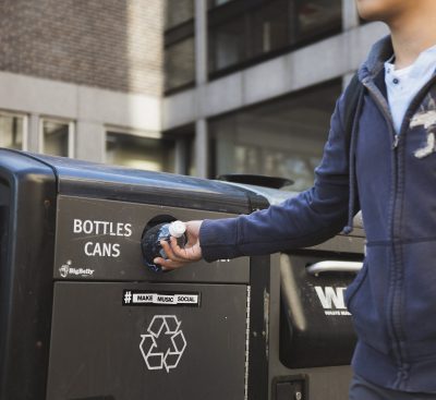 A student puts an empty water bottle into a recycling receptacle in front of the George Sherman Union