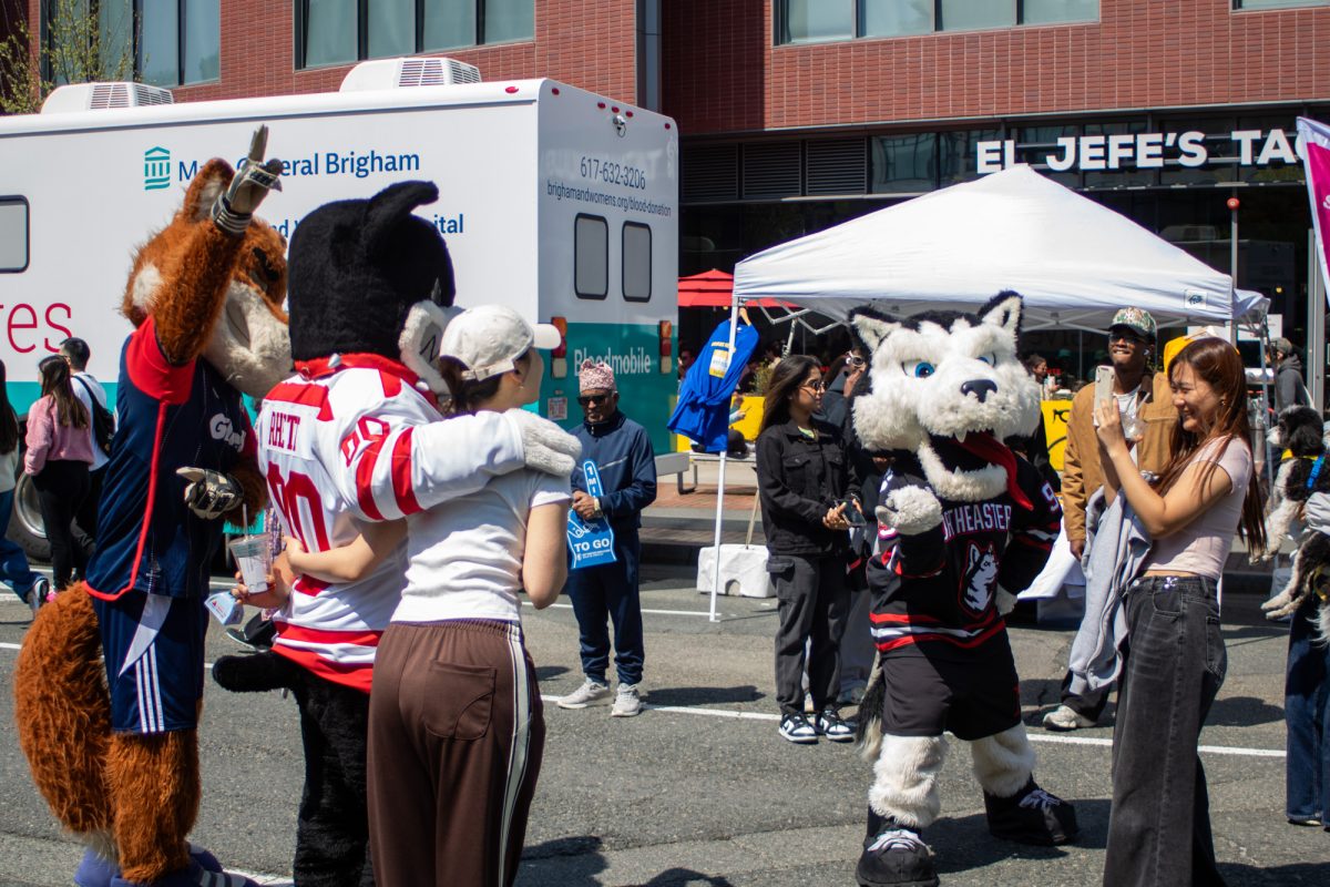 Rhett and New England Revolution mascot Slyde take a photo with a marathon spectator as Northeastern University mascot Paws watches on. 