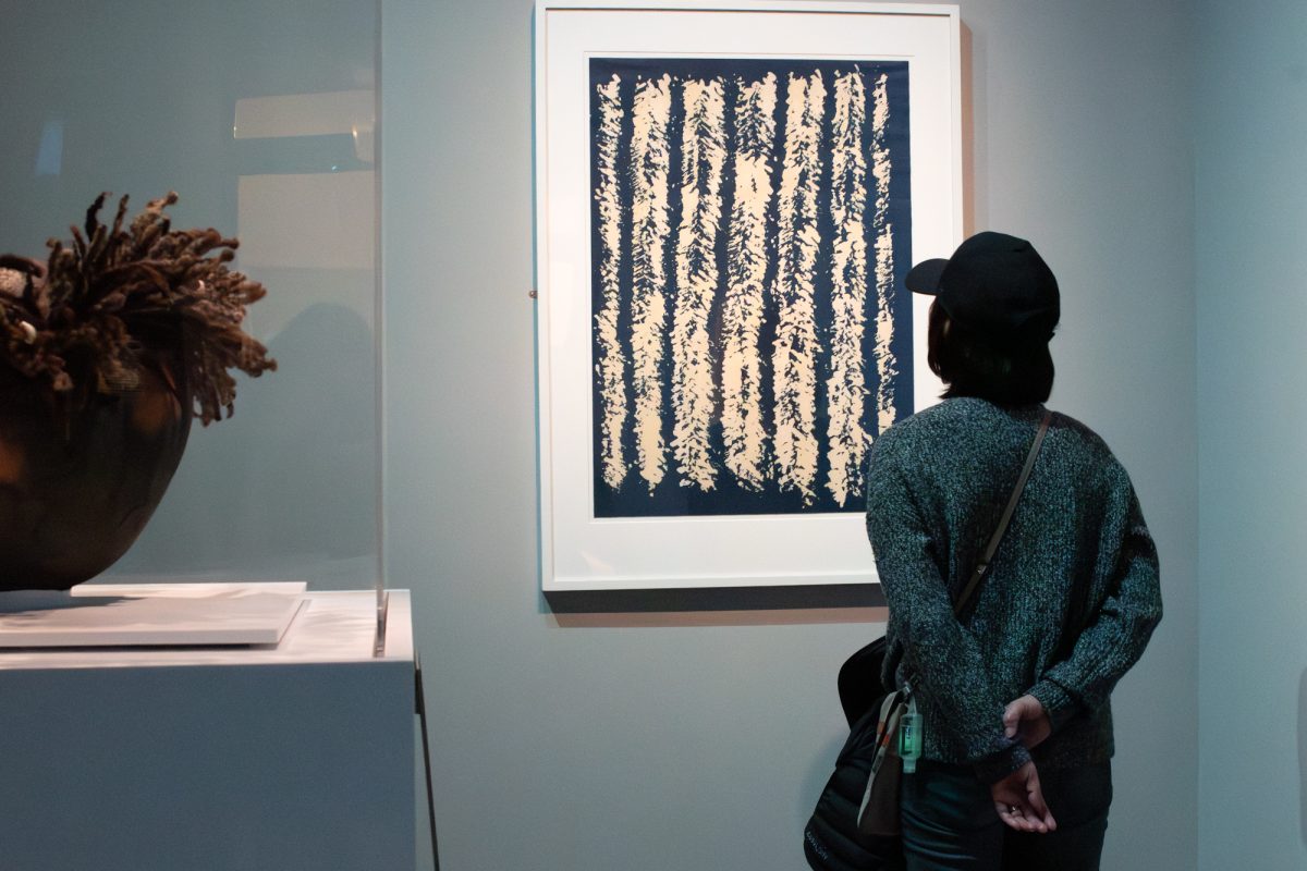 A museum-goer views “Indigo Between Cornrows,” a two-color lithograph by artist Sonya Clark, at the exhibition.
