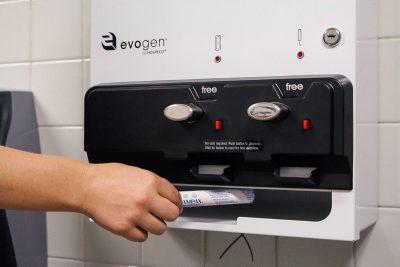 A hand reaching to grab a tampon out of a feminine product dispenser