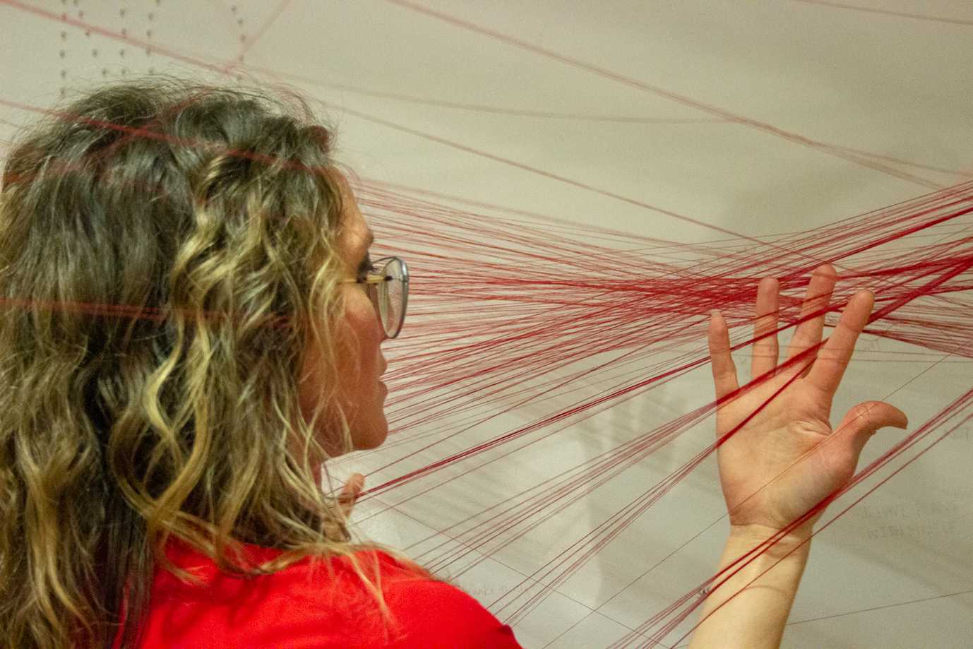 Artist Marika Whitaker examines threads strung by participants as part of her art installation, “CONSENT,” which is on display at an exhibition space in Cambridge. HANNAH EDELMAN/ DFP STAFF