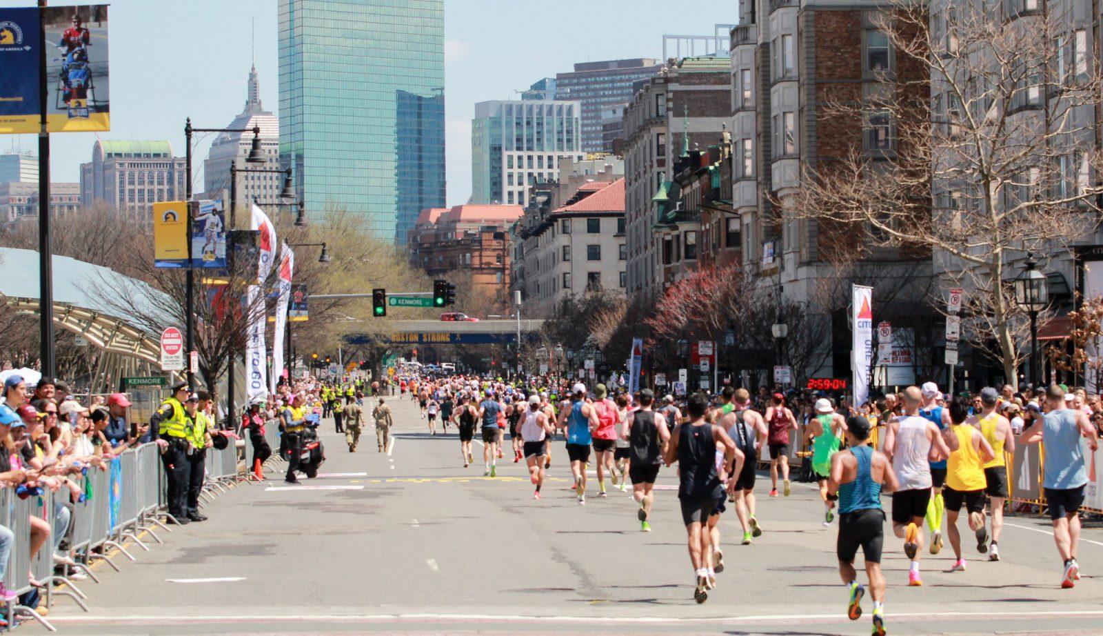 Boston Marathon participants run through Kenmore Square as people watch behind barricades on Monday. SARAH CRUZ/DFP PHOTOGRAPHER