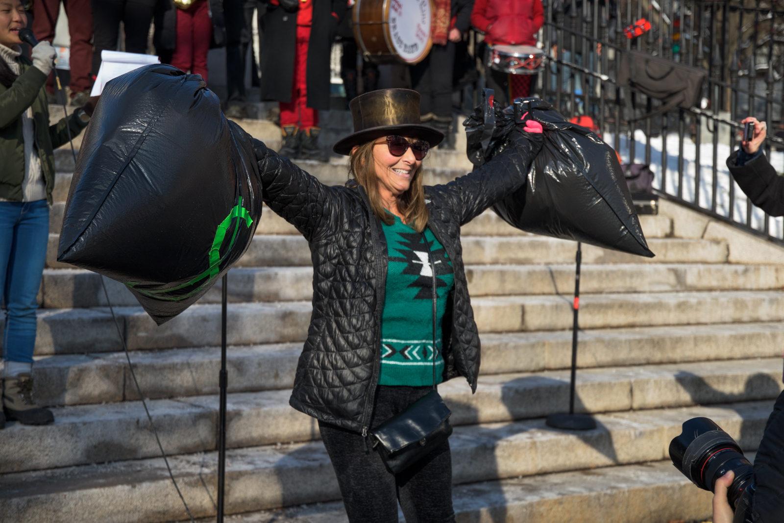 A Stop the GOP Tax Bill rally attendee holds up fake bags of money as she pretends to represent the 0.1 percent. PHOTO BY CHLOE GRINBERG/ DAILY FREE PRESS STAFF