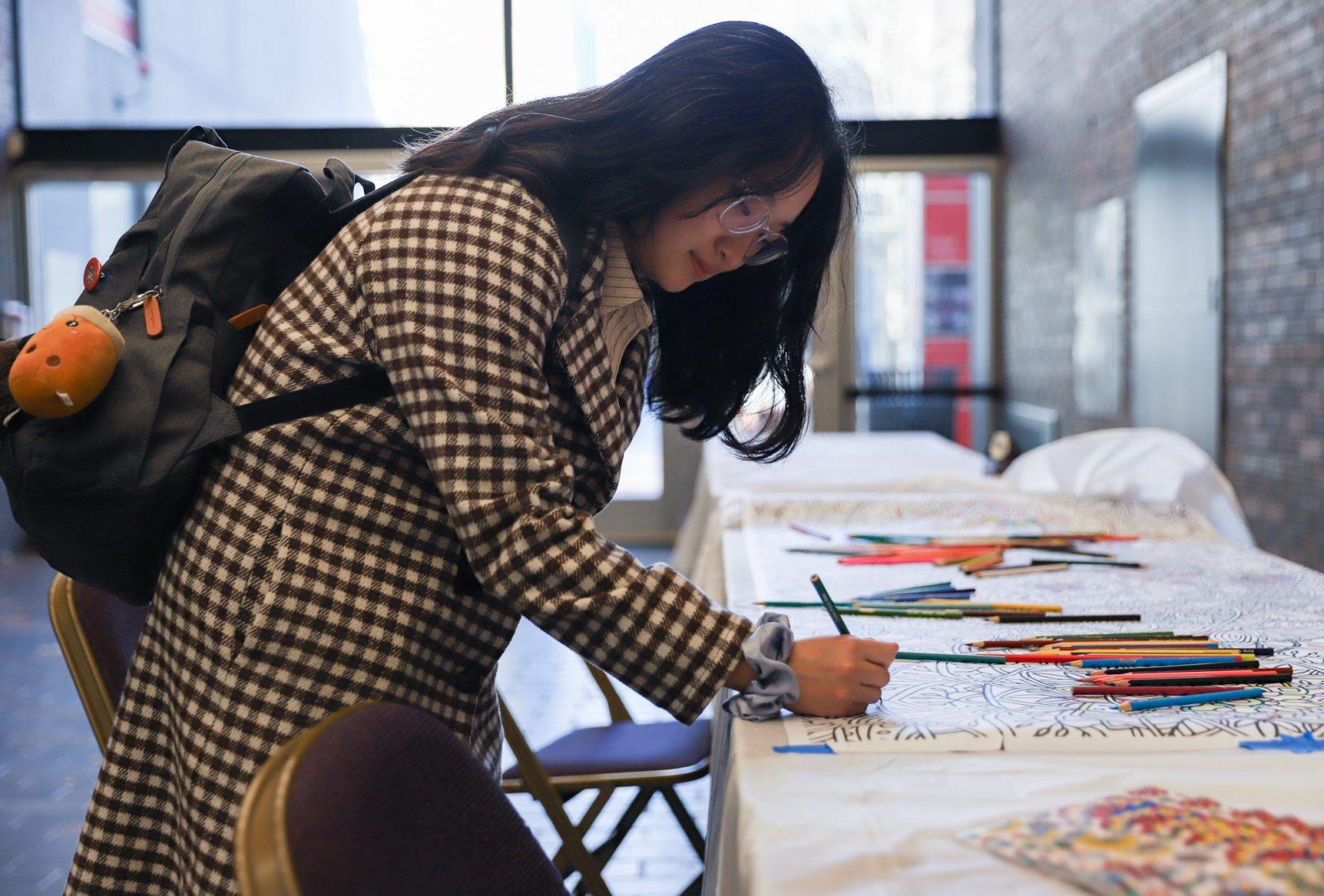 Xiaodan He (CAS '25) colors in a large coloring sheet splayed out on a table in the George Sherman Union Link for Student Wellbeing's decompression activity, "Pause from Politics: Connection and Coloring." Boston University Student Health Services offered in-person and online mental health services and activities for students following the 2024 presidential election. KATE KOTLYAR/DFP PHOTOGRAPHER  
