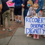 Child holding a sign reading "Recovery deserves dignity"