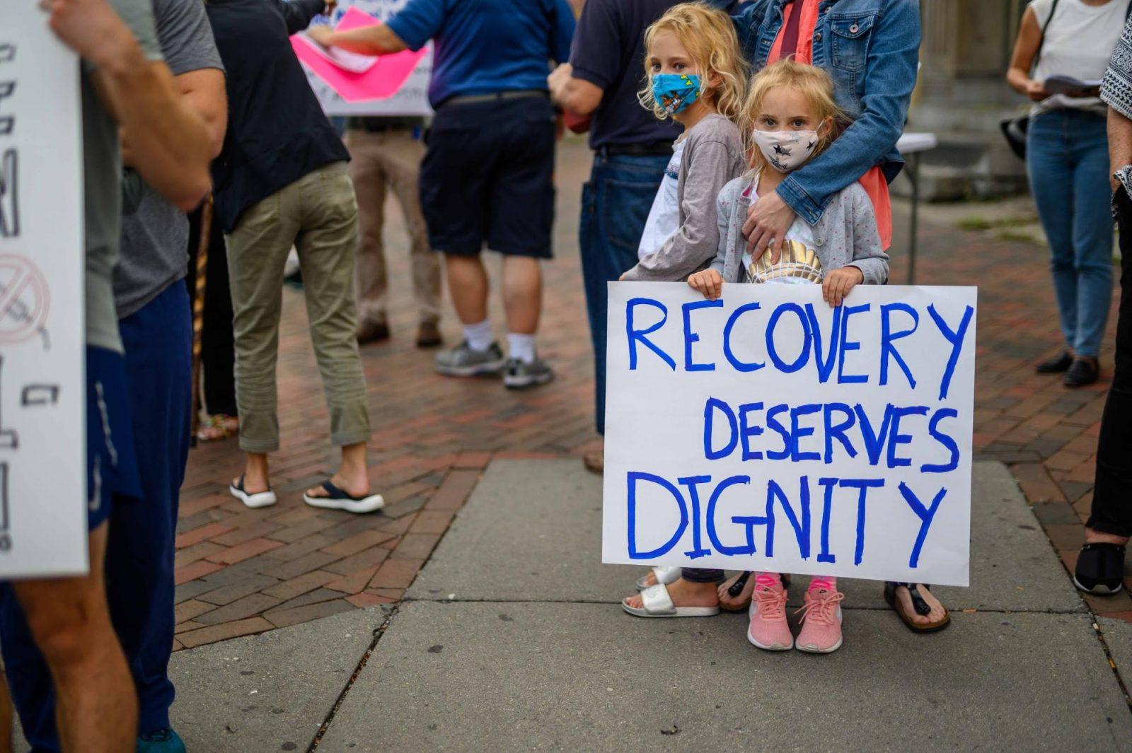 Child holding a sign reading "Recovery deserves dignity"