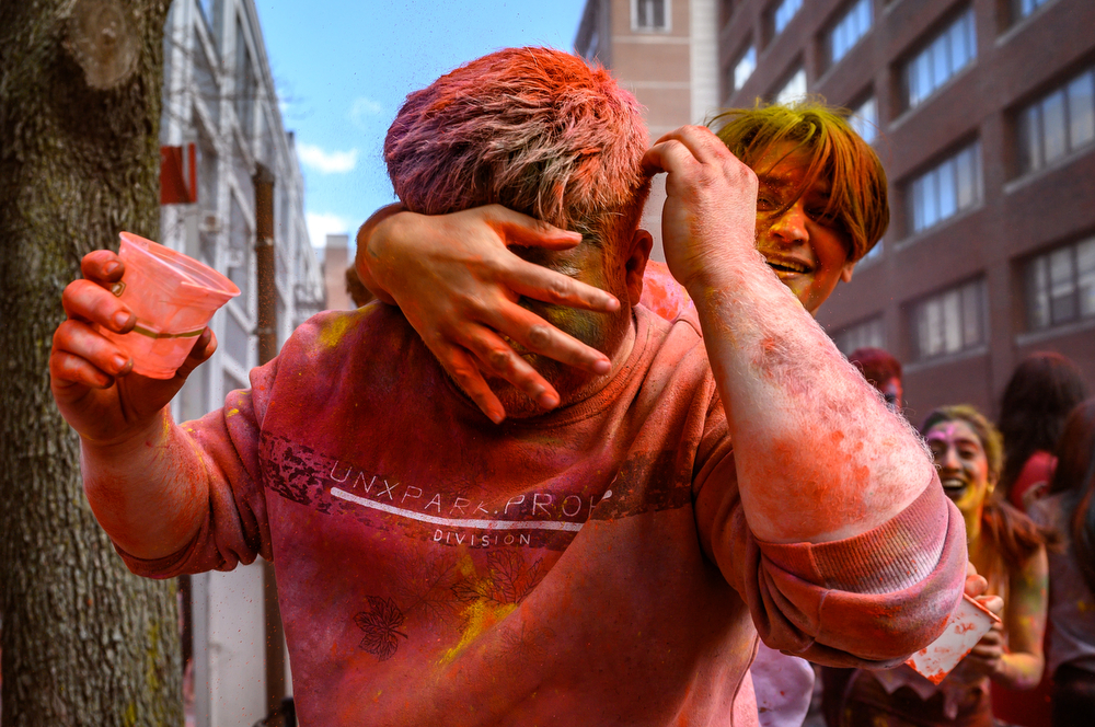 A participant grabs his friend from behind to cover him in orange powder.