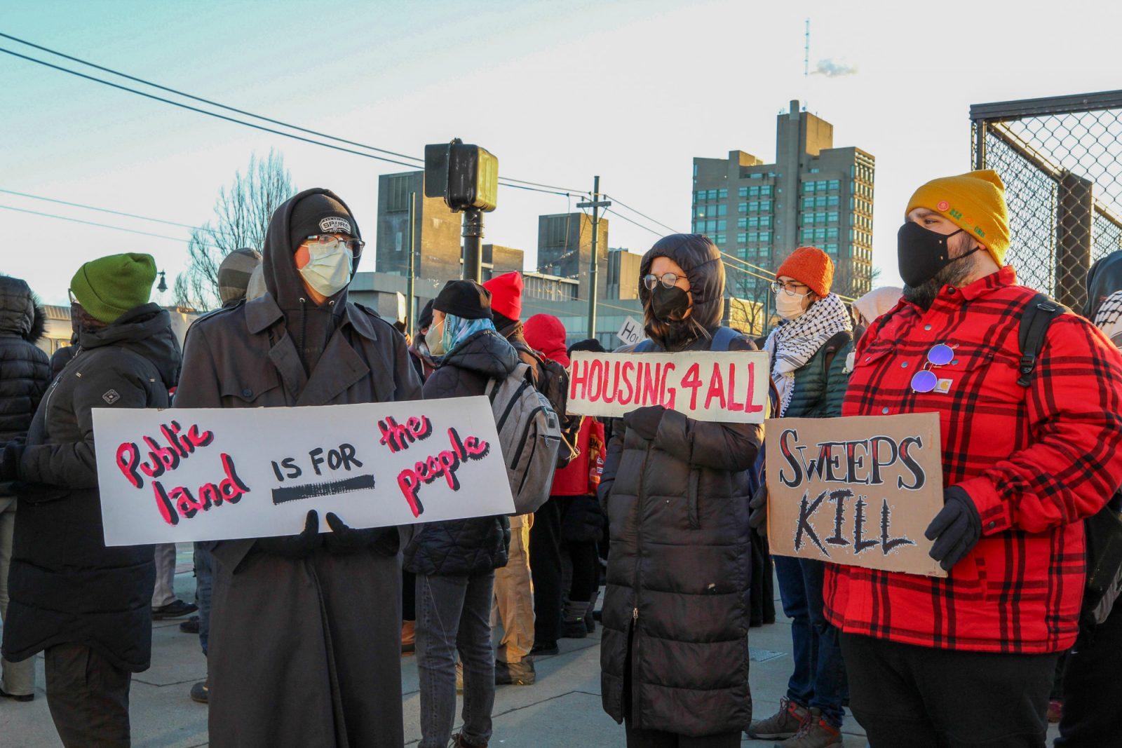 Protestors hold signs against homeless encampment sweeps on the corner of Commonwealth Avenue and the Boston University Bridge. Warm Up Boston, an organization that supports Boston’s unhoused community, organized a rally to stop the sweeps of homeless encampments on Wednesday morning. SARAH CRUZ/DFP PHOTOGRAPHER 
