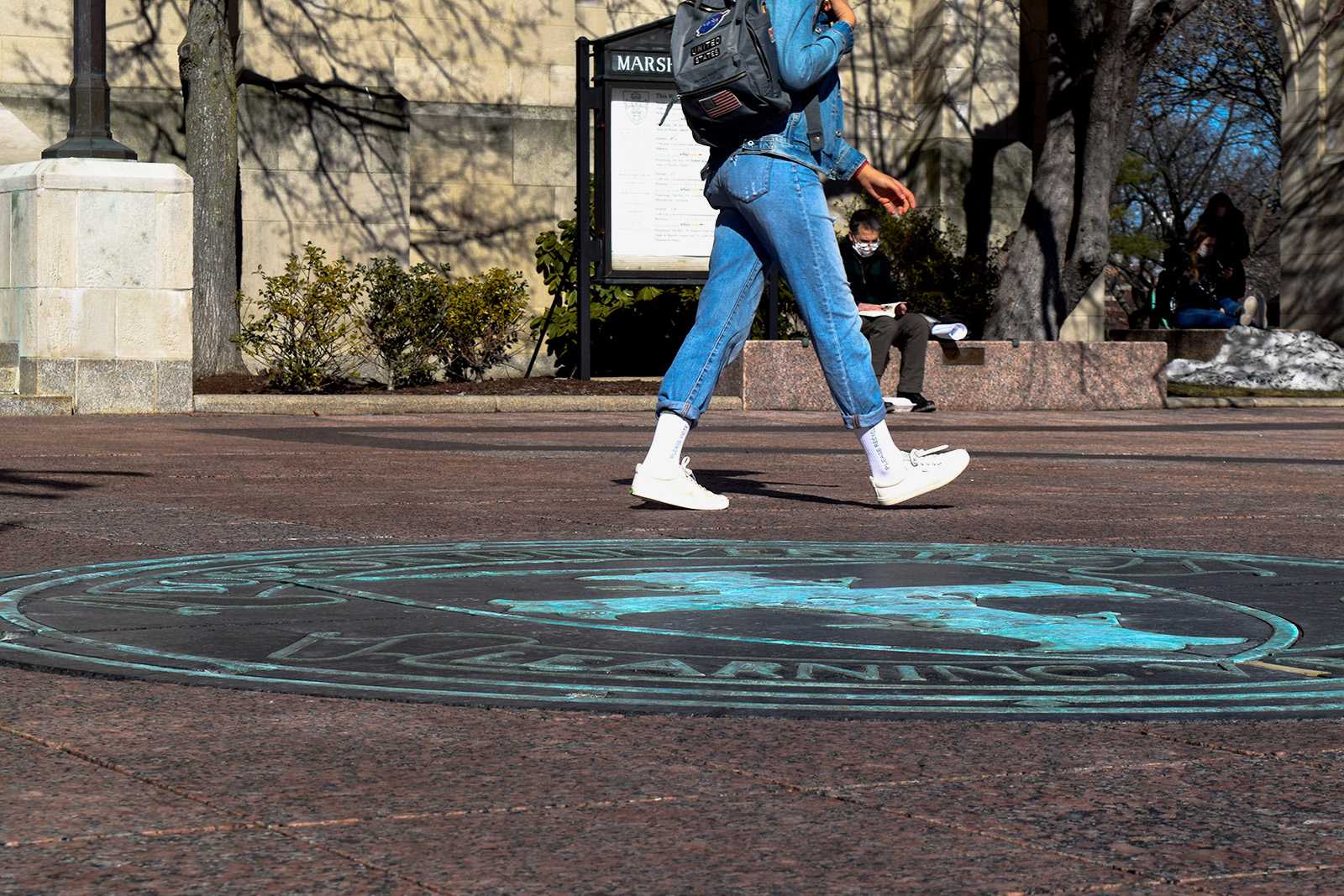 Person walks by the BU seal in MArsh plaza