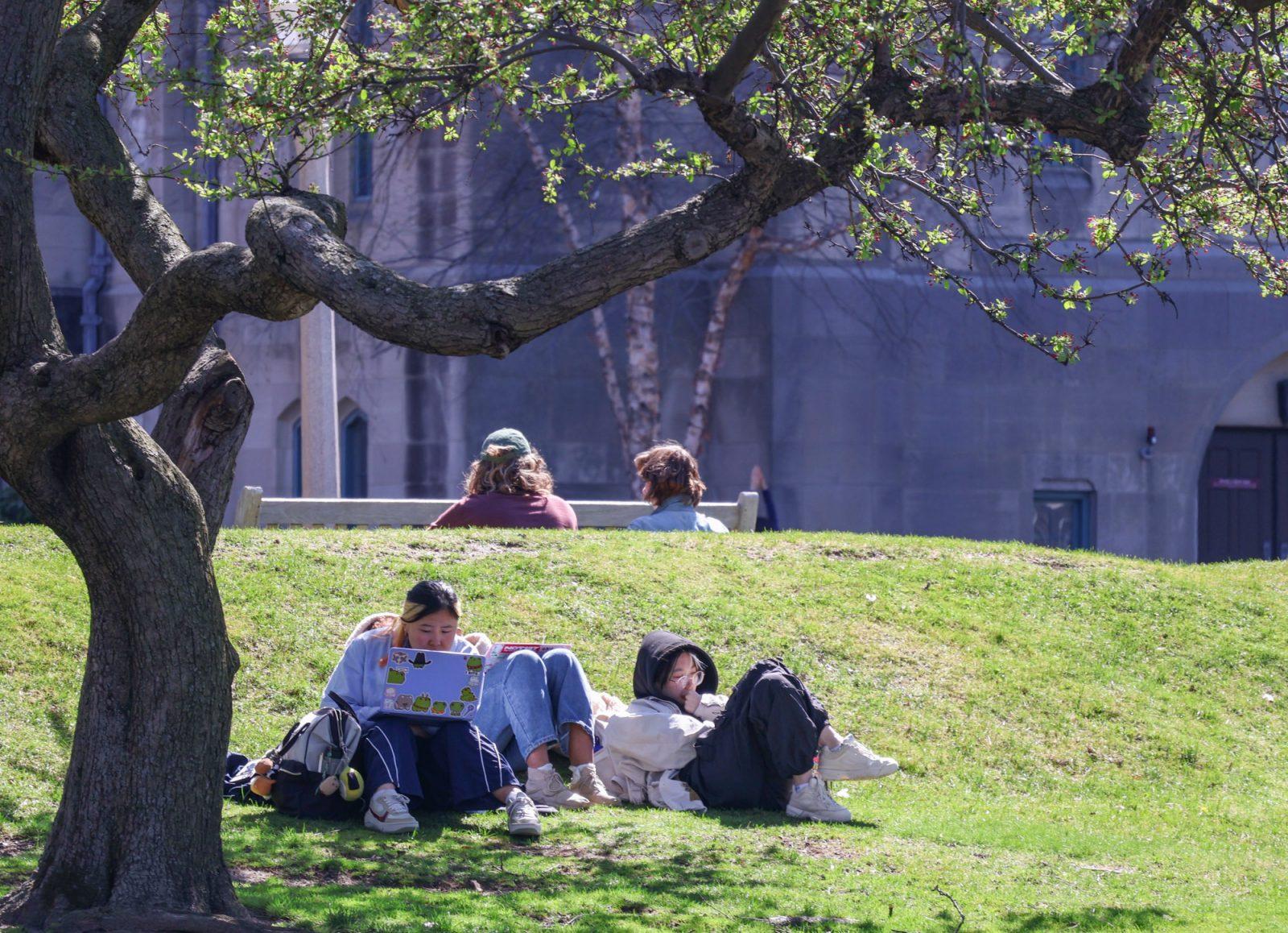 From left: Junior Angie Chen, freshman Kirstin Smith and sophomore Emerson Gray work on assignments while laying in the grass on BU Beach. ZOE KU/DFP PHOTOGRAPHER