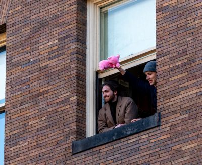 Two people looking out from a window. One is holding a pink stuffed animal in their hand