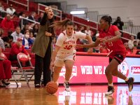 Women's basketball player dribbles away from an opponent while coach watches