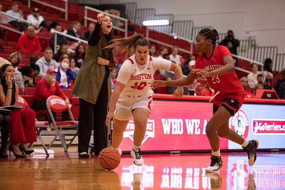 Women's basketball player dribbles away from an opponent while coach watches