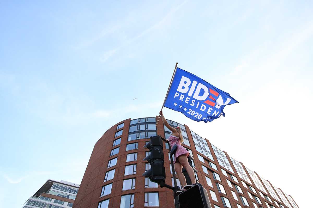 A person holding a Biden flag stands on a traffic light Nov. 7, 2020 near the Boston Public Garden. Boston University students shared mixed opinions regarding the Biden administration’s first year in office. MEGHAN SCOTT/ DFP FILE
