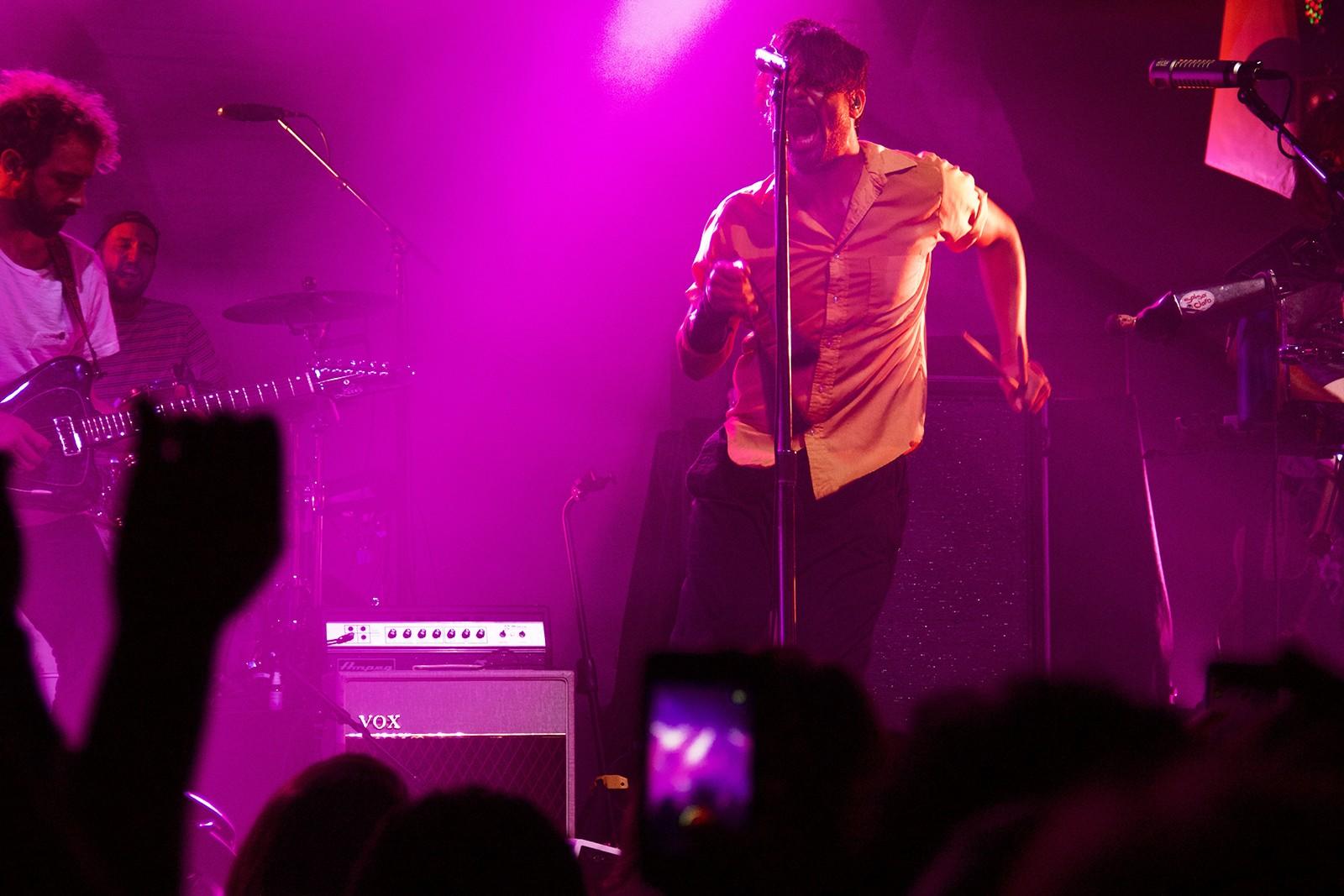 Holding a set of drumsticks, Sameer Gadhia of Young the Giant takes a break from playing the small set of drums next to him and sings to the crowd. PHOTO BY OLIVIA FALCIGNO/ DAILY FREE PRESS STAFF