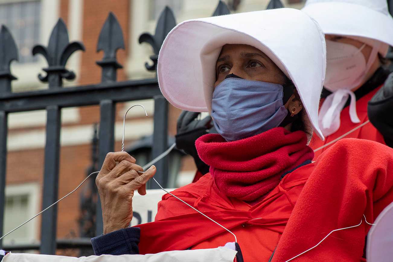 A protester dressed as a handmaid stands outside the Massachusetts State House in support of the Act to Remove Obstacles and Expand Abortion Access on Oct. 25. The Massachusetts House of Representatives will vote on a budget amendment this week that, if passed, will expand abortion access. SHANNON DAMIANO/ DAILY FREE PRESS STAFF


