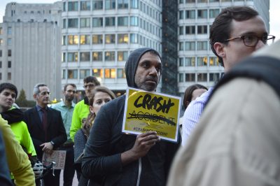 Surrounded by bikers wearing yellow in solidarity with the dead, onlookers listen to a speaker call for faster action, at the Streets Are For People rally Thursday evening in City Hall Plaza. PHOTO BY CAROLYN KOMATSOULIS/ DAILY FREE PRESS CONTRIBUTOR