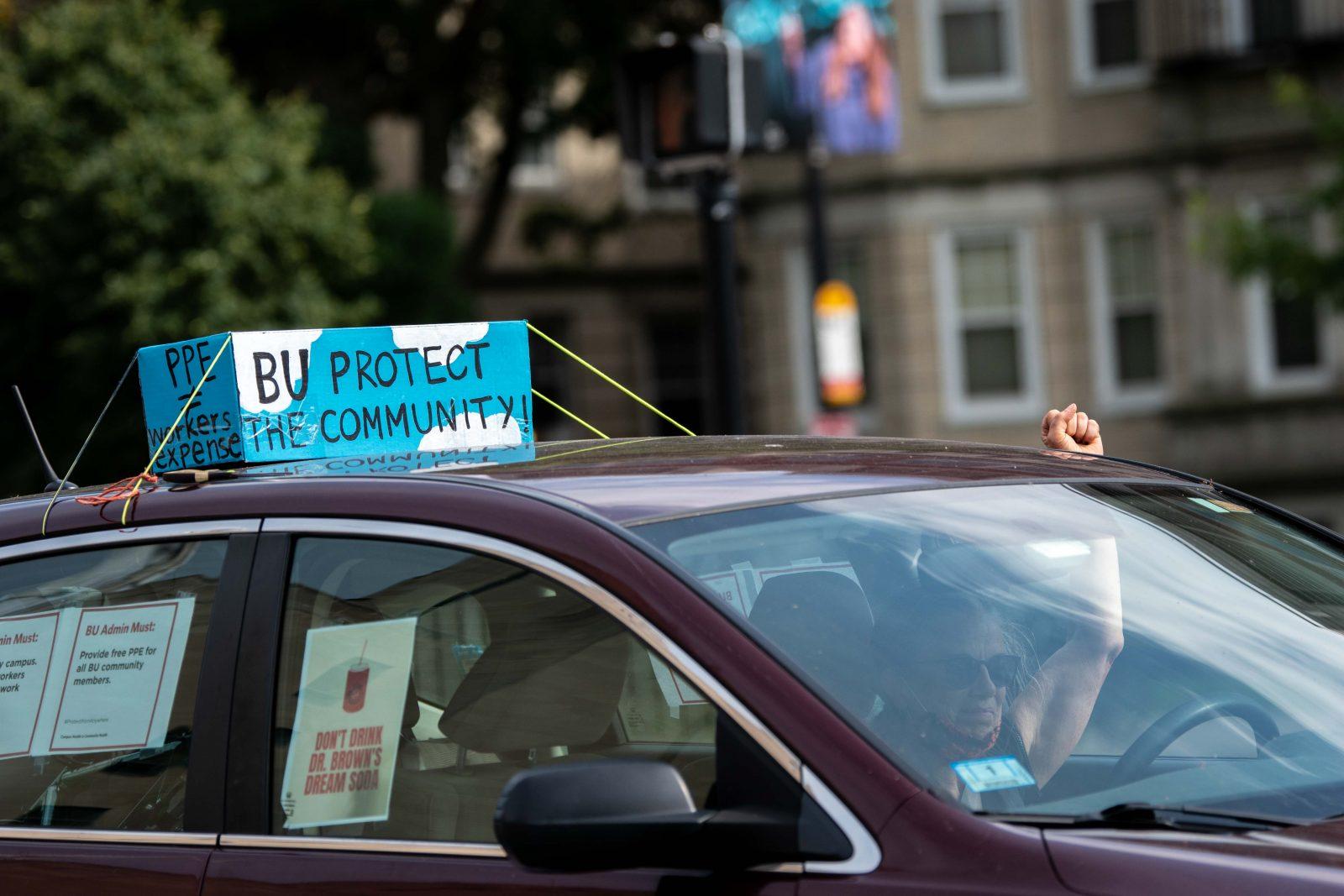 A demonstrator raises their fist as they drive through the Boston University campus. Cyclists, pedestrians and drivers participated in Thursday’s Protest From Anywhere urging the University to allow staff to work from home, provide free personal protective equipment and give free testing to local residents. LAURYN ALLEN/ DAILY FREE PRESS STAFF
