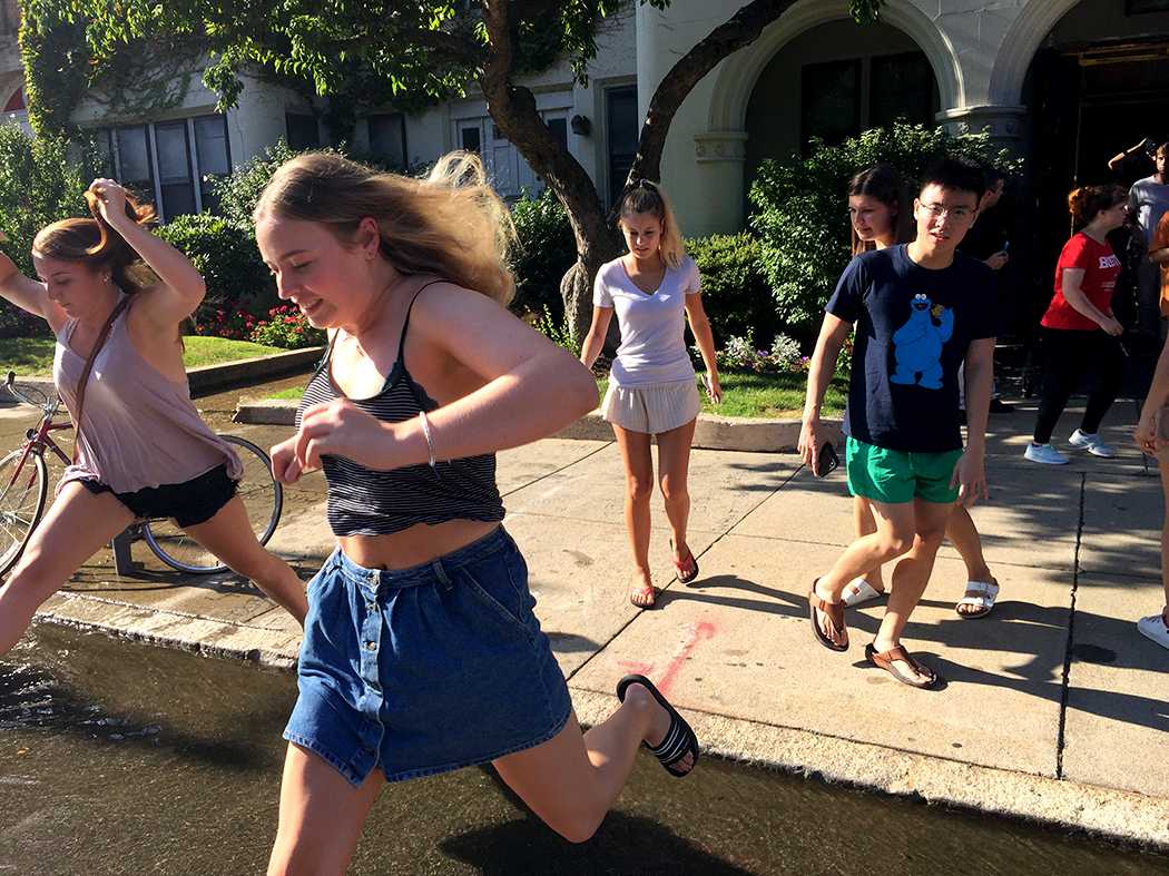 Students jump over water coming from a pipe in Danielsen Hall after evacuating the dorm. A fire on the ninth floor of Danielsen caused the evacuation Tuesday. PHOTO BY VIVIAN MYRON/ DAILY FREE PRESS STAFF