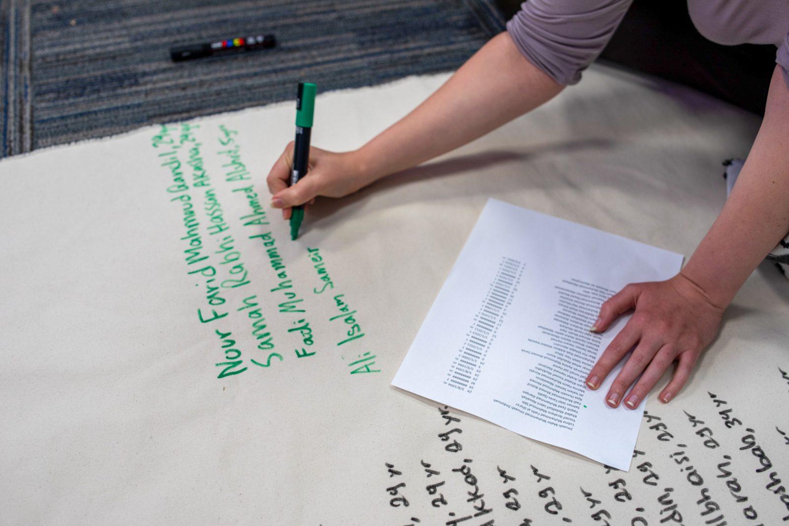 A person writes the names of Palestinians who were killed in Gaza. Boston University Students for Justice in Palestine is holding multiple events this week for the anniversary of Oct. 7, including the writing of the names of victims. BARRETT WALSH/DFP PHOTOGRAPHER 