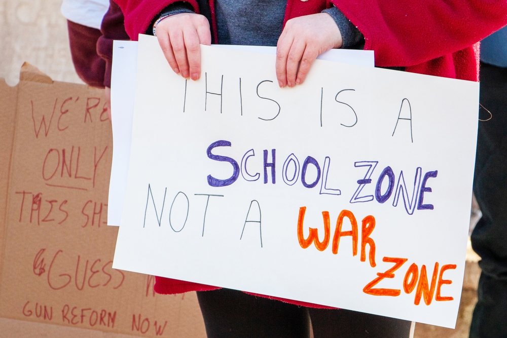 A rally attendee holds a sign that reads, “this is a school zone not a war zone.”
