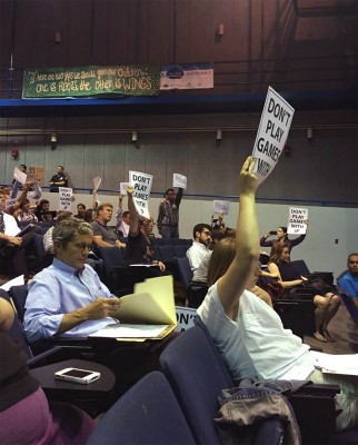 Protesters hold up signs at the sixth Boston 2024 community meeting Tuesday night. PHOTO BY JUSTIN PALLENIK/DAILY FREE PRESS STAFF