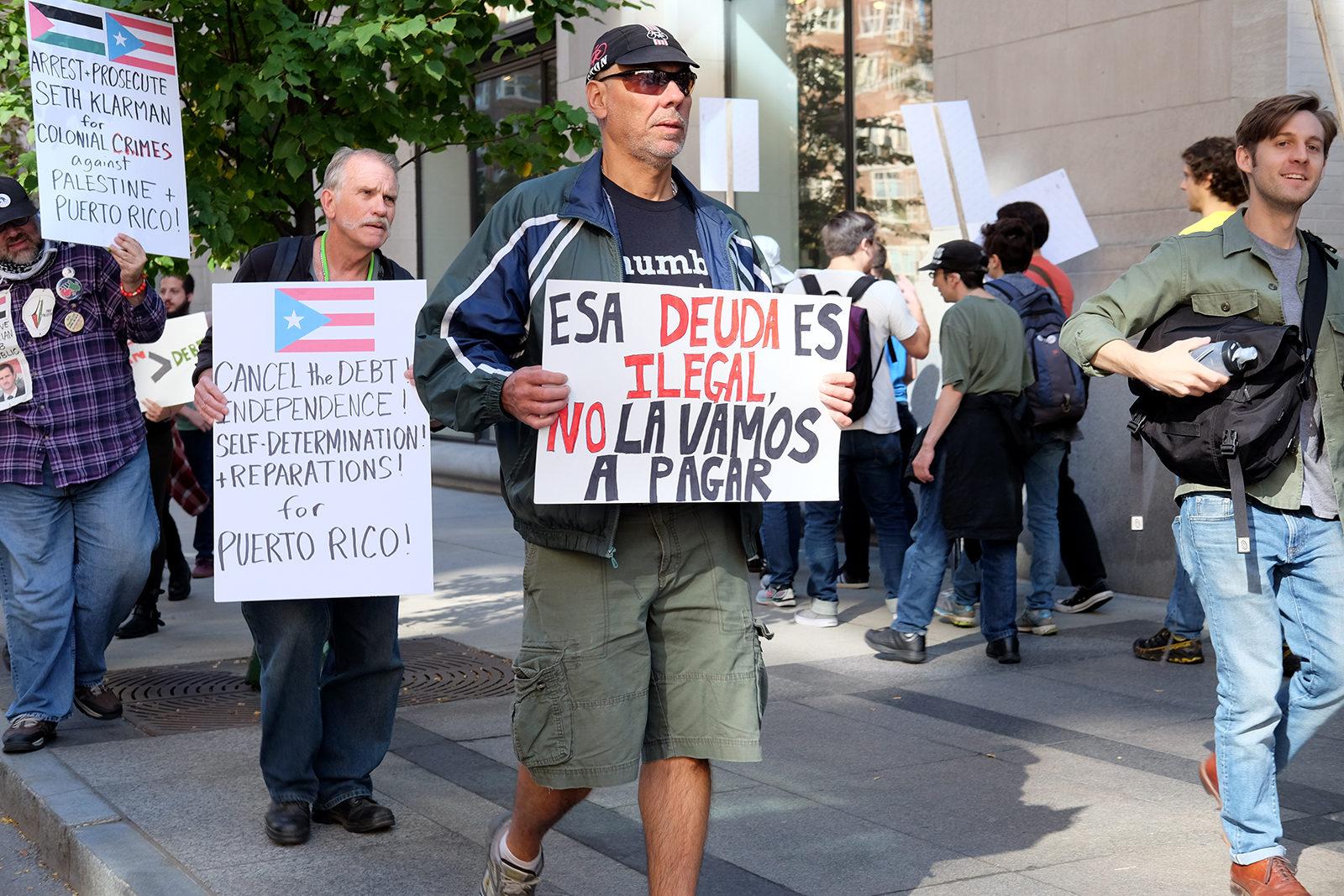 A protester carries a sign Saturday afternoon at a rally against the Baupost Group, one of the largest holders of Puerto Rican debt. PHOTO BY ISABELLA ARTEAGA/ DAILY FREE PRESS STAFF