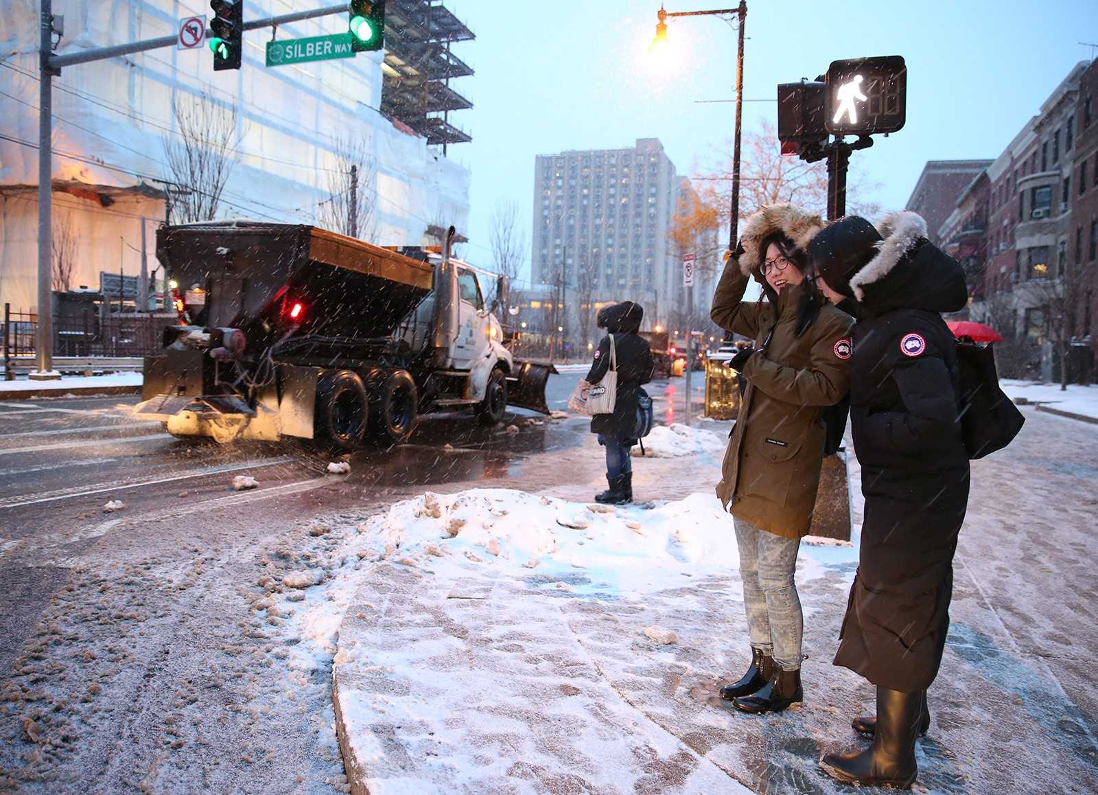 Lizhen Fu, a junior in the Questrom School of Business, and Bijun Zhou, a junior in the College of Arts and Sciences, observe a brigade of snow removal trucks as they brave the storm Monday afternoon. PHOTO BY SARAH SILBIGER/DAILY FREE PRESS STAFF